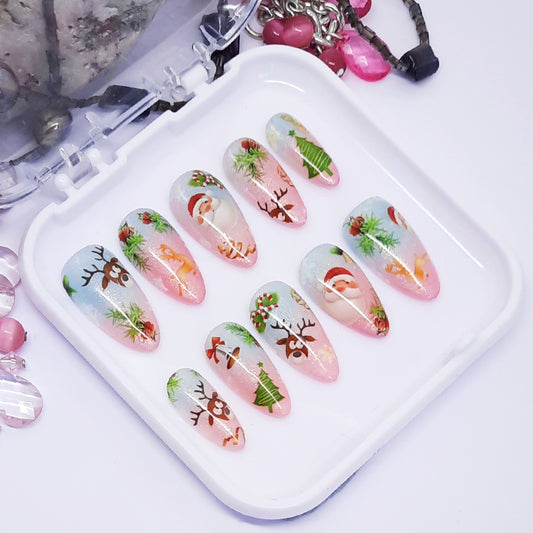 A set of pink and blue ombre press on nails with a cute Christmas themed design, displayed in a white tray on a white background.