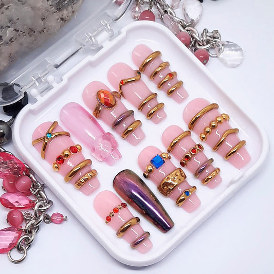 Set of pink and gold nail art decorations on a white tray with jewelry.