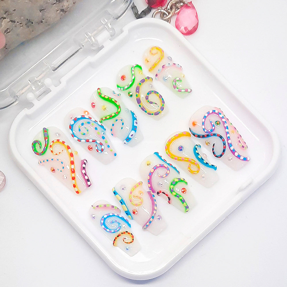 A set of white press on nails with a colourful 3d design, displayed in a white tray on a white background.