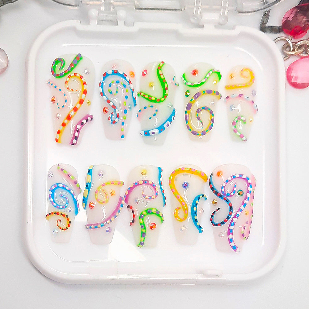 A set of white press on nails with a colourful 3d design, displayed in a white tray on a white background.