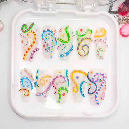 A set of white press on nails with a colourful 3d design, displayed in a white tray on a white background.
