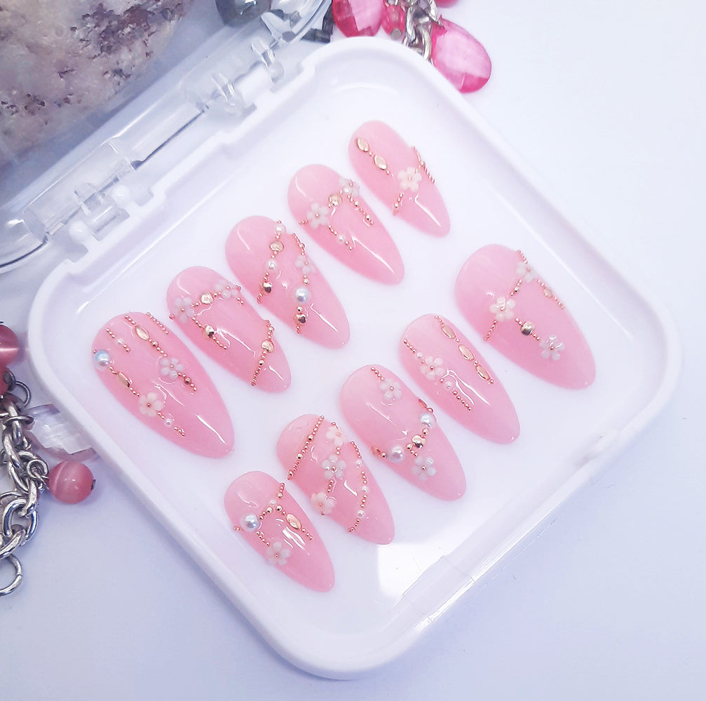 A set of pink press on nails with a 3d design resembling daisy chains Displayed in a white tray on a white background.
