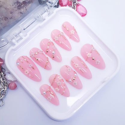A set of pink press on nails with a 3d design resembling daisy chains Displayed in a white tray on a white background.