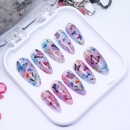 A set of pink and blue themed press on nails with a floral and butterfly design displayed in a white tray n a white background.