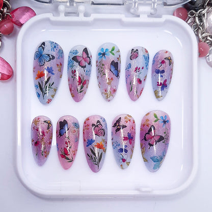 A set of pink and blue themed press on nails with a floral and butterfly design displayed in a white tray n a white background.