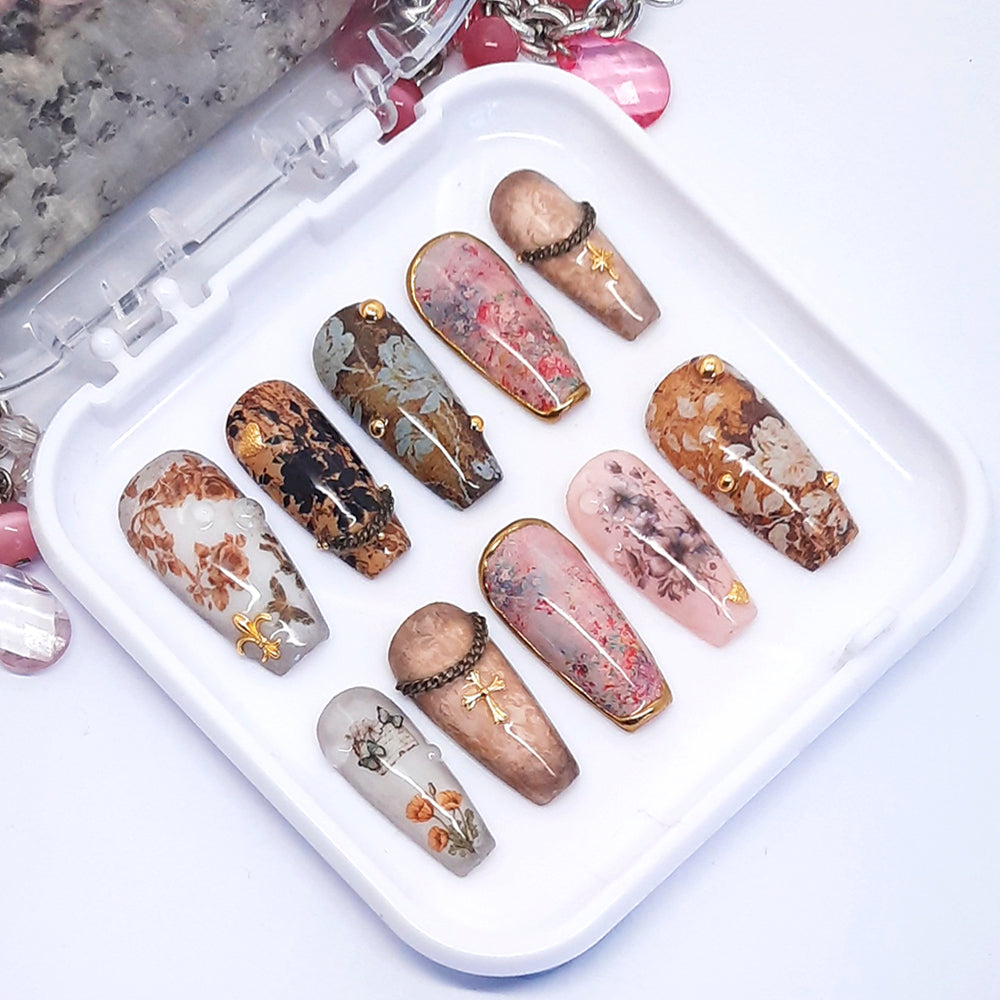 A set of decorative press on nails in a brown floral design displayed in a white tray.