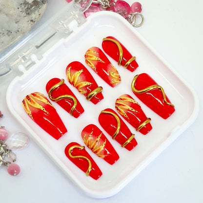 Red nail art designs with gold accents on a white tray.