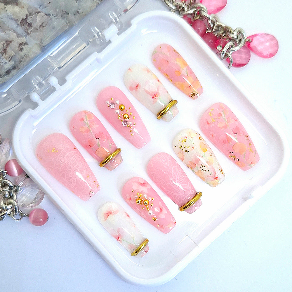 Set of pink and white press on nails with floral and lace design with gold chrome bangles and 3d nail art. Displayed in a white tray on a white background.