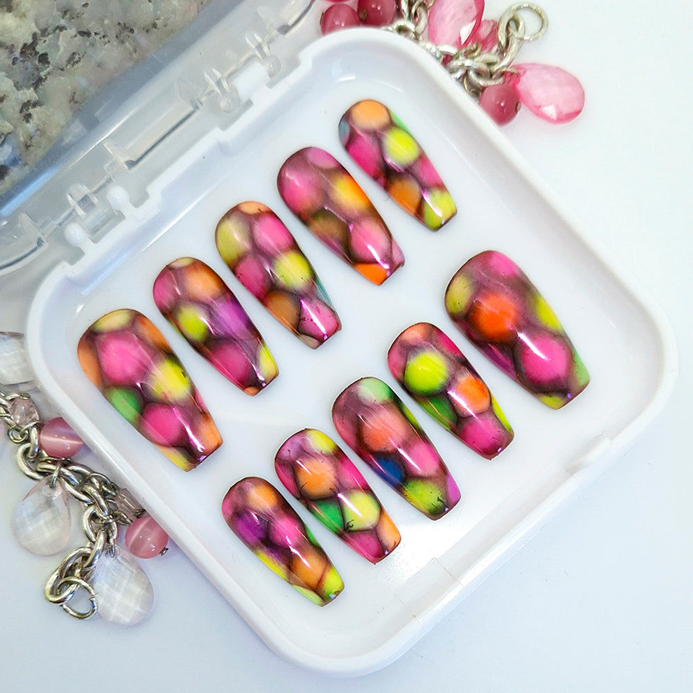 A set of very colourful medium coffin press on nails with a design of multi-coloured patches and finished with a chrome sheen. Displayed in a white tray on a white background.