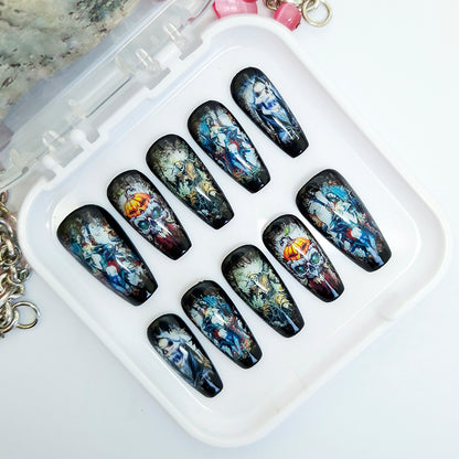 A set of ten coffin-shaped press-on nails with dark, gothic fantasy illustrations, displayed in a white plastic case on a white surface.